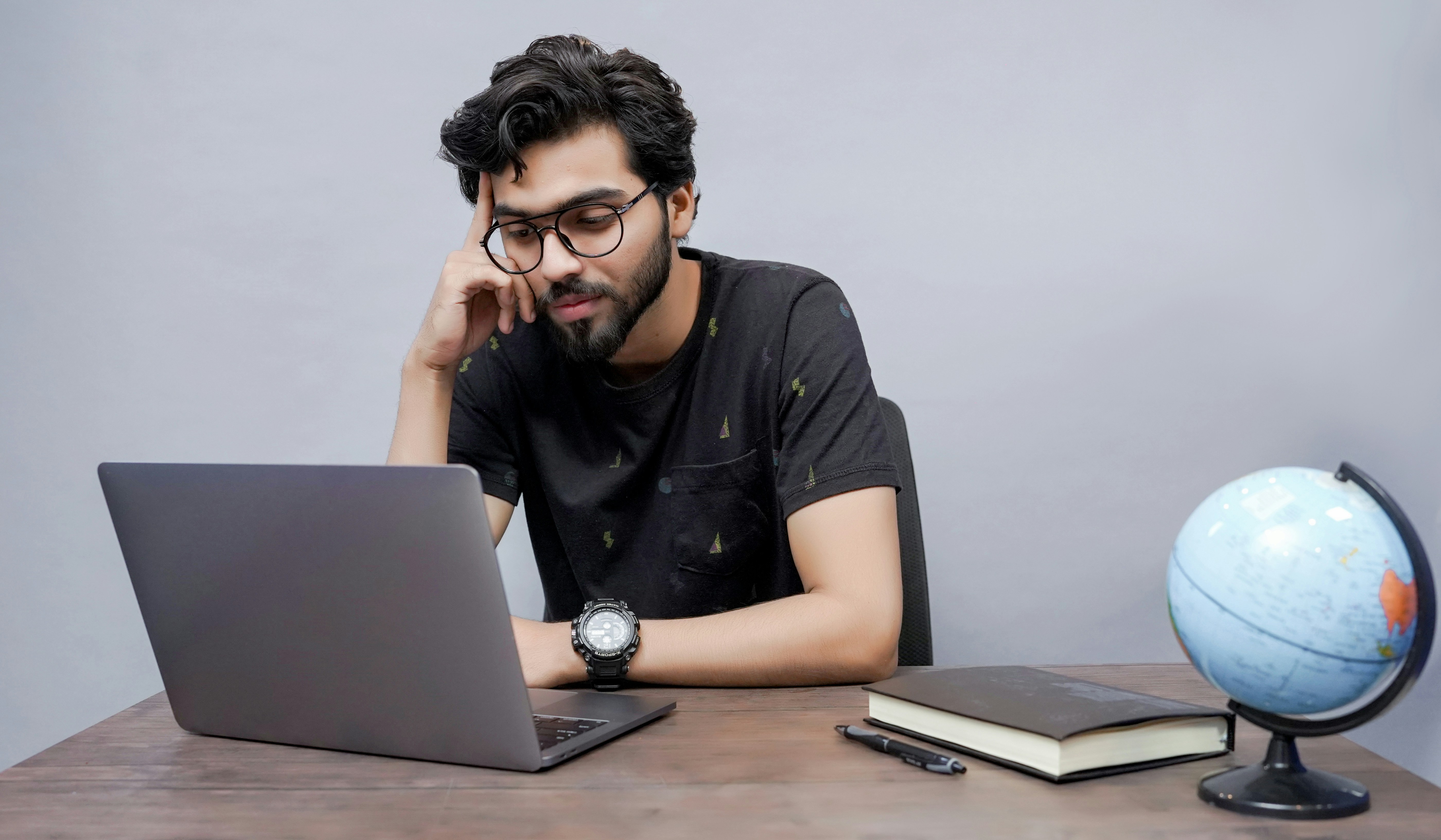 Indian Student at a desk with laptop, notebook and globe.