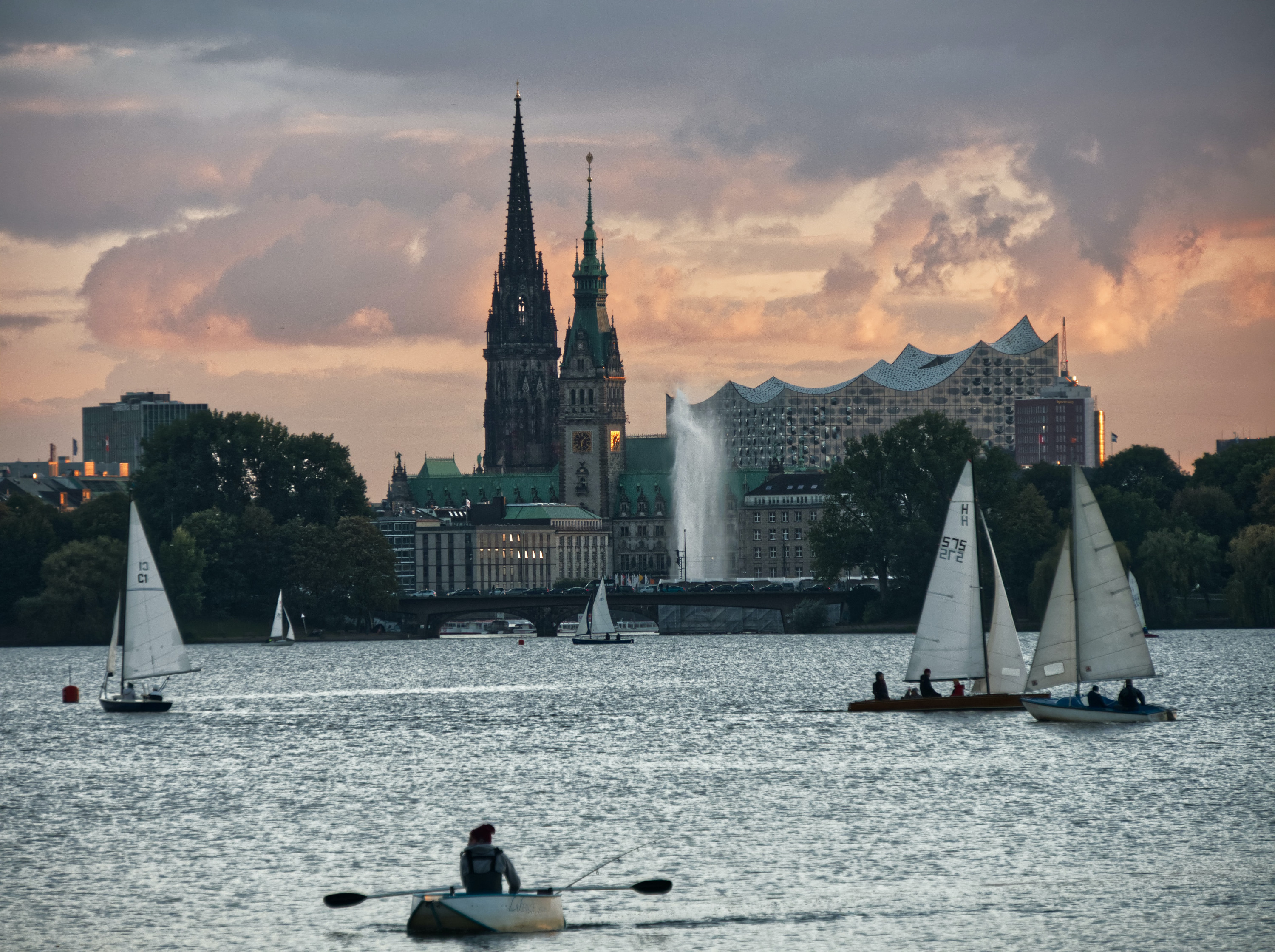 Blick über die Hamburger Alster auf Rathaus und Elbphilharmonie, im Vordergrund einige Segelboote.